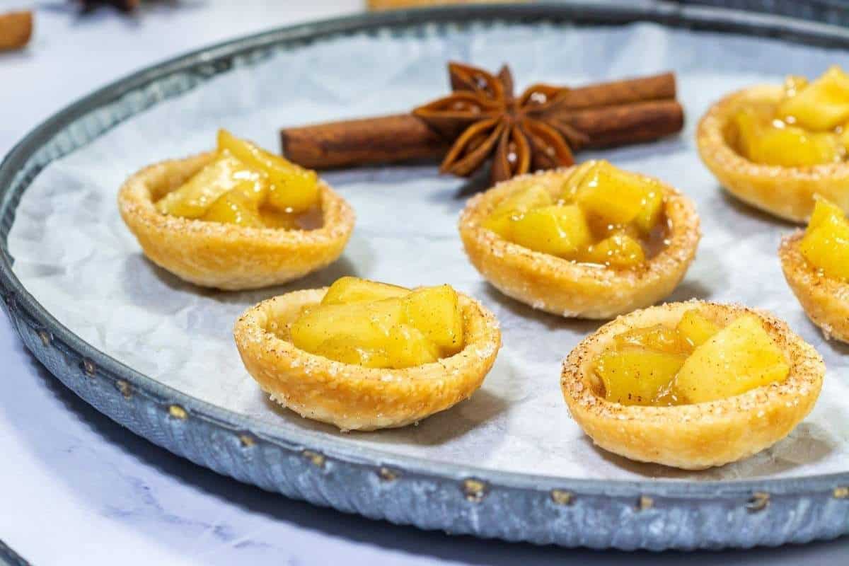 Bite-sized caramel apple tartlets arranged on a serving plate.
