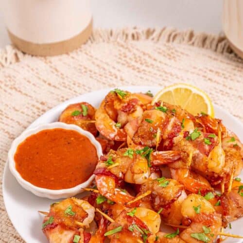 Delicious bacon wrapped shrimp served with a side of tangy dipping sauce and lemon wedge, perfect for seafood.