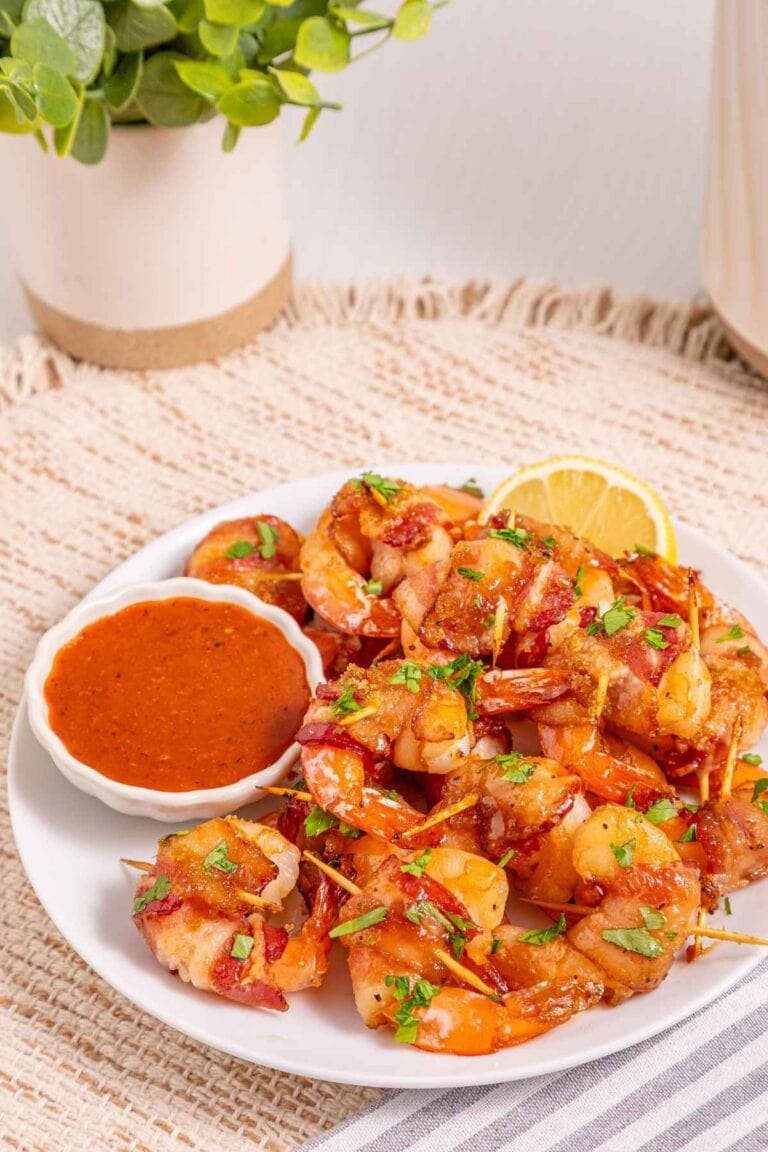 Delicious bacon wrapped shrimp served with a side of tangy dipping sauce and lemon wedge, perfect for seafood.