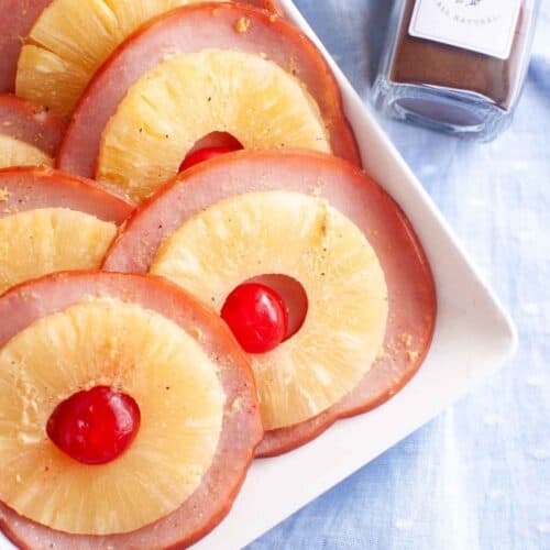 A white plate with slices of glazed ham is arranged neatly.