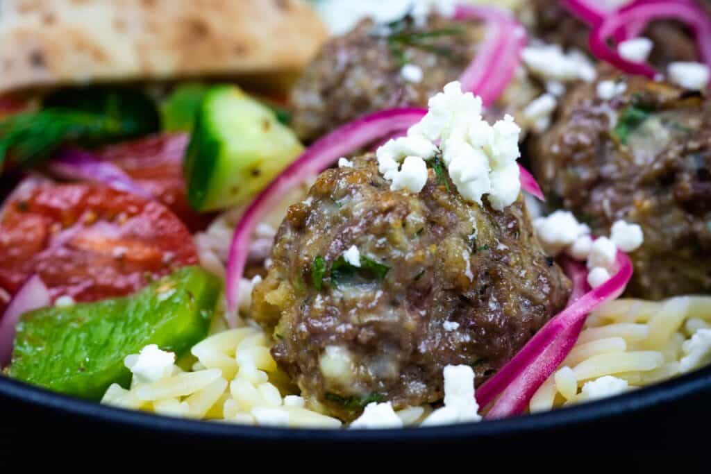 A close-up shot of lamb meatballs with tzatziki served in a bowl alongside rice and other sides.