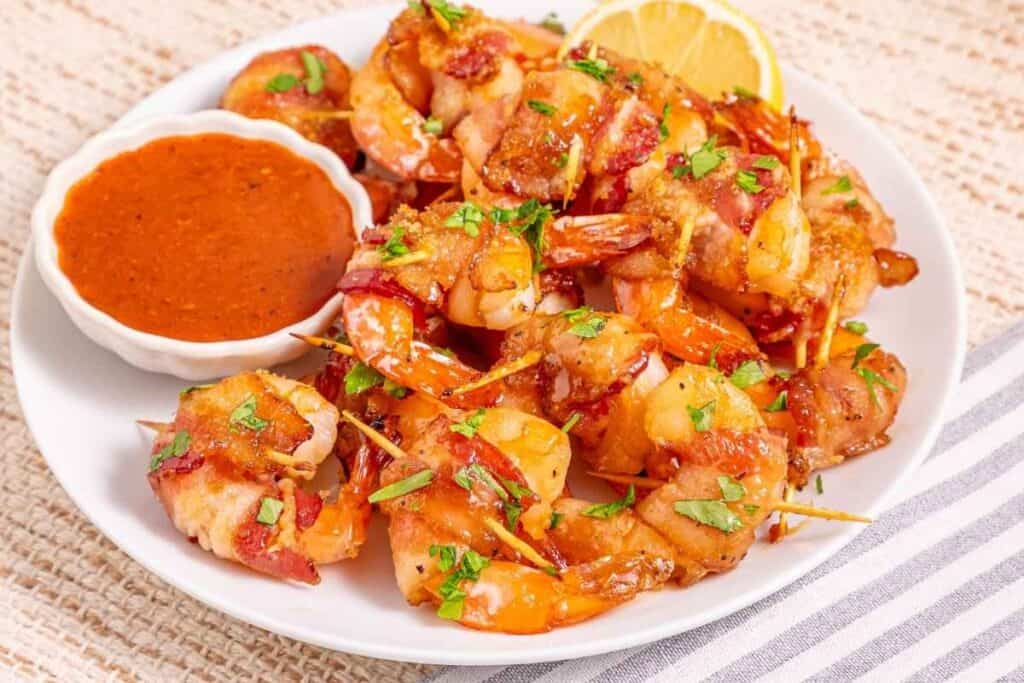Delicious bacon wrapped shrimp served with a side of tangy dipping sauce and lemon wedge, perfect for seafood.