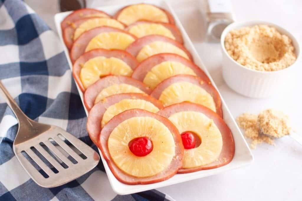 Slices of glazed ham are arranged neatly on a white plate.