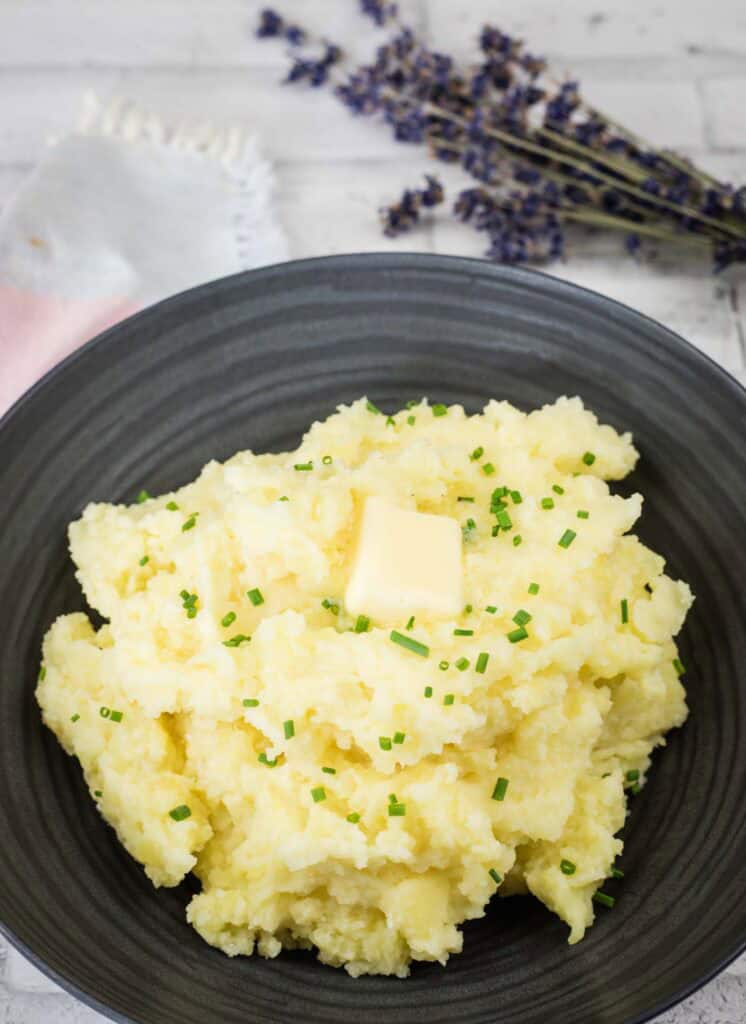Mashed potatoes on a black plate topped with chopped chives and butter.