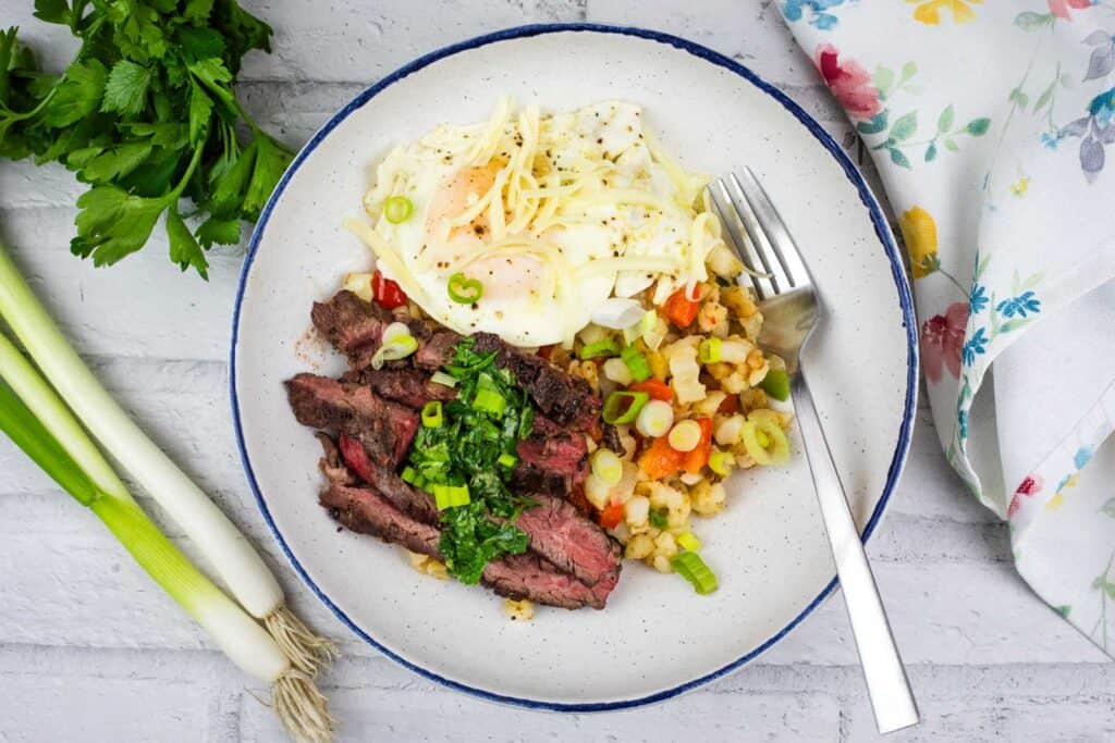 A top-down view of a Steak and Eggs Breakfast Bowl, placed next to celery, parsley, and a napkin.