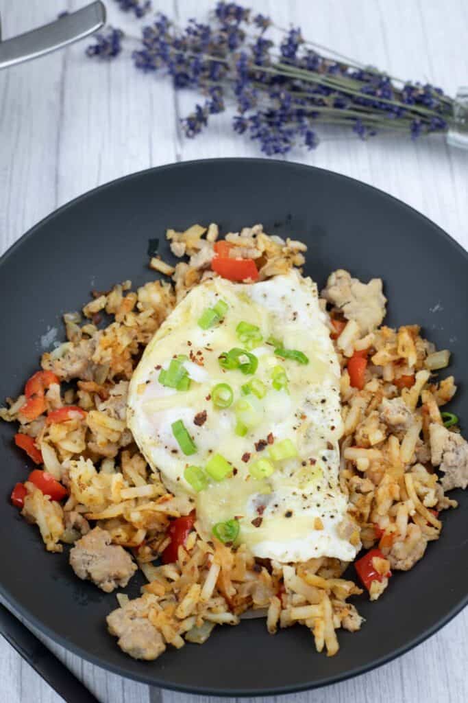 A black plate with a Turkey Sausage Breakfast Bowl topped with green onions and egg.