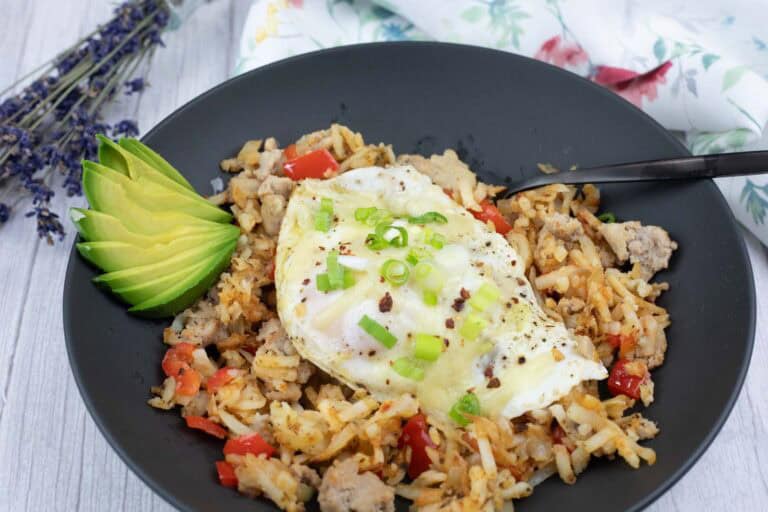 A black plate holds a Turkey Sausage Breakfast Bowl, accompanied by sliced avocado, topped with an egg and green onions.