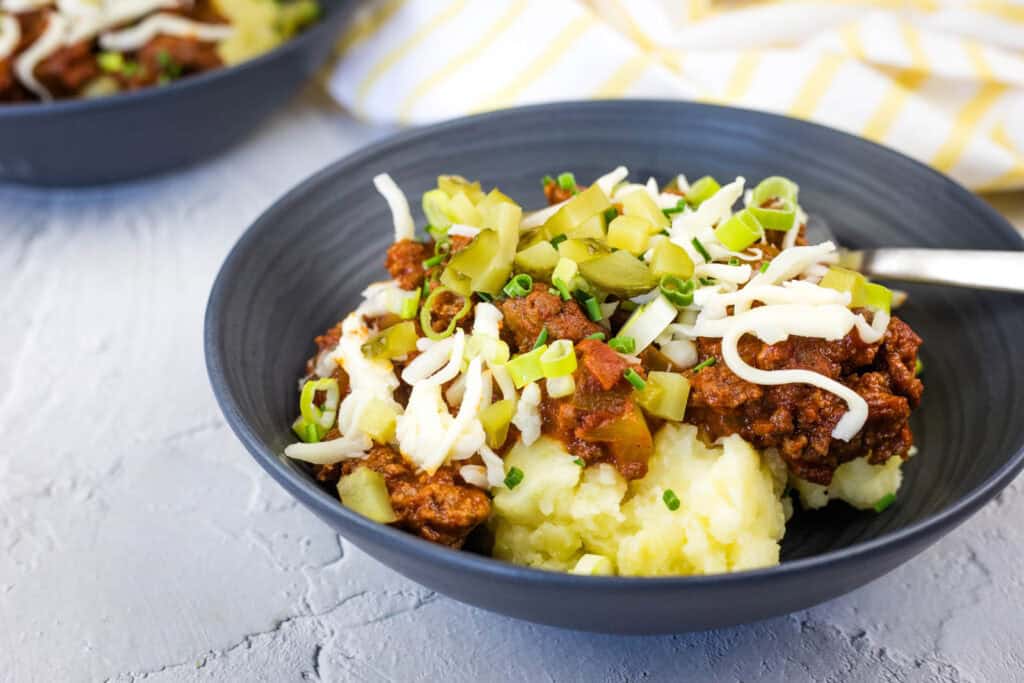 A black bowl filled with Sloppy Joe Mashed Potato topped with cheese and bell pepper.