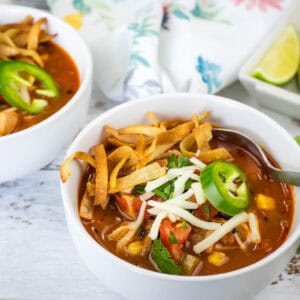 Close-up of chicken tortilla soup with cheese and jalapenos in a white bowl.