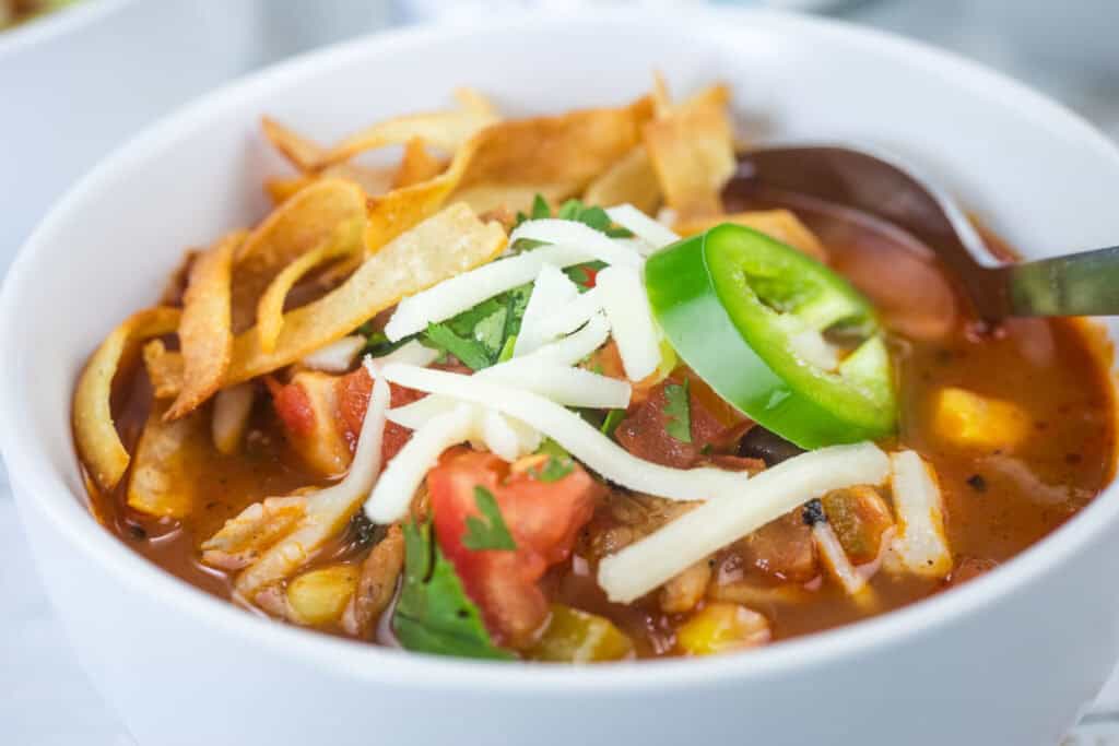 A close-up shot of Chicken Tortilla Soup, featuring a spoon in a bowl.